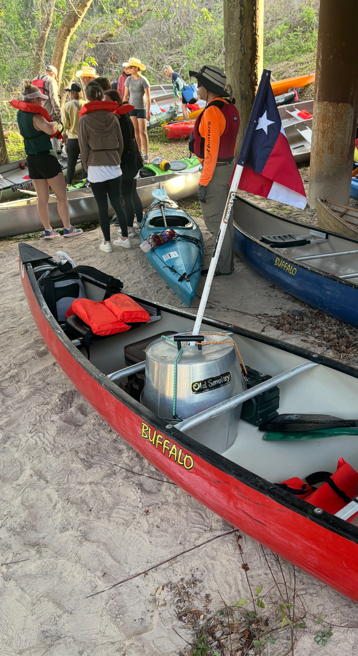 A red kayak with an Old Smokey Charcoal Grill in it. The grill has a Texas Flag attached.